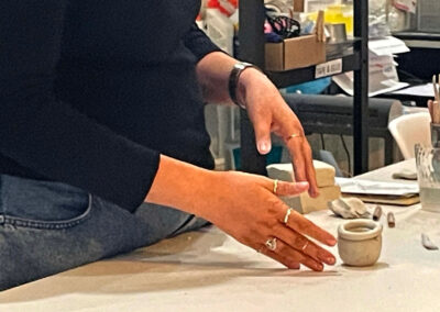a persons hands point to a small fist sized pot in the frame. the person is wearing rings and instructing on how to create a pinch pot