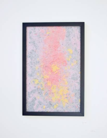 A framed abstract artwork featuring a blend of pink, yellow, and gray colors displayed on a white wall.