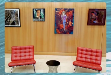 Two red chairs and a small round table sit in front of a wooden wall displaying five colorful paintings in a modern interior space.