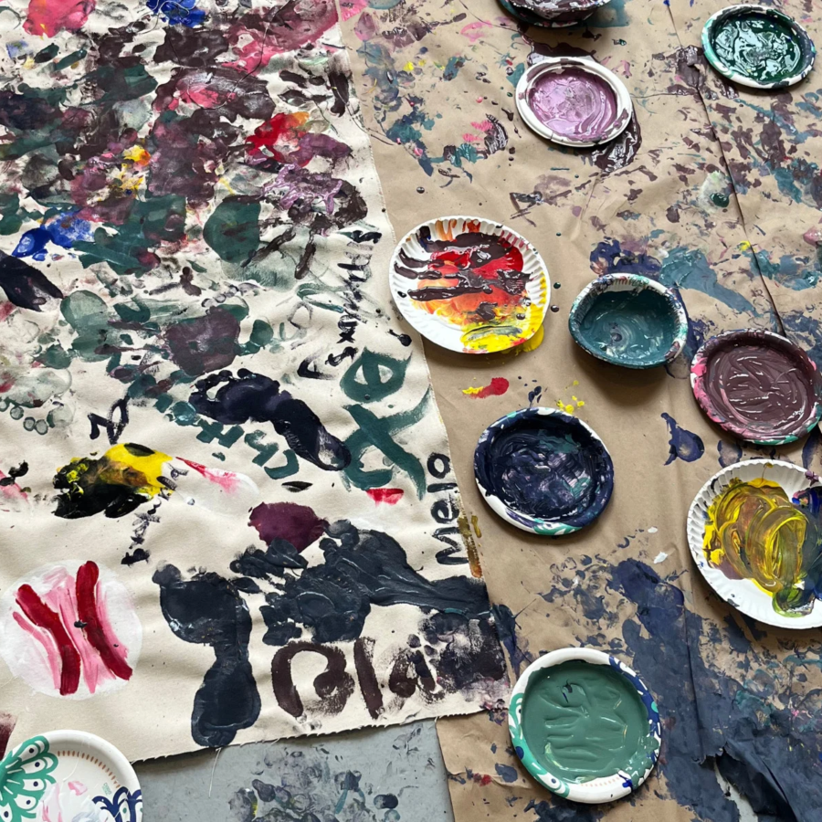 Paint-splattered paper with colorful painted plates and artwork scattered on a messy floor covering.