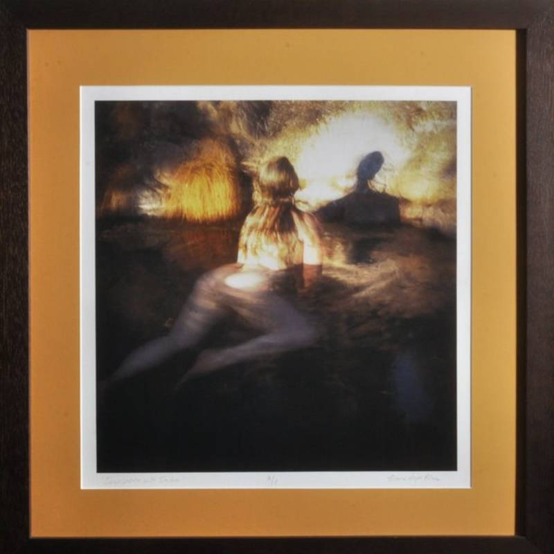A framed print depicting two blurred, partially submerged human figures in dark water with an illuminated background.