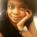 Christina Bourne is a Black woman with an afro, wearing a black top, and leaning her head on her hand while looking at the camera.