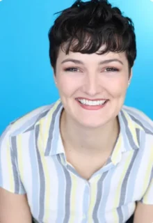 Leah Huskey has short dark hair and is wearing a striped, collard shirt while smiling at the camera.