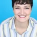 Leah Huskey has short dark hair and is wearing a striped, collard shirt while smiling at the camera.