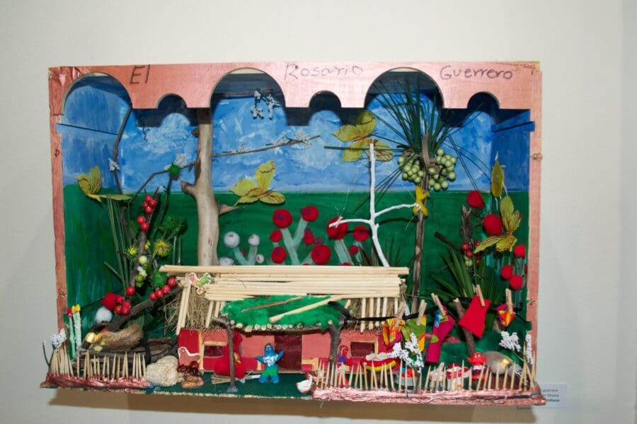 A colorful handmade diorama features a rural scene with trees, plants, and various small figures, labeled "El Rosario Guerrero" at the top.